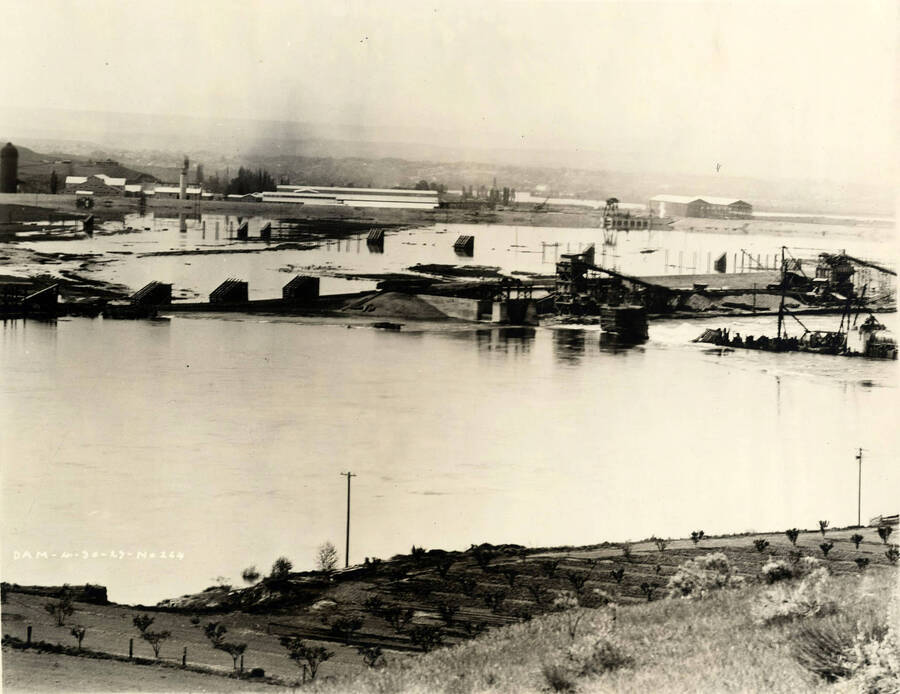 A view of the construction of the Lewiston Dam. In the background is the Lewiston Mill. Written on the photograph is 'Dam 4/30/1927 No. 264.'