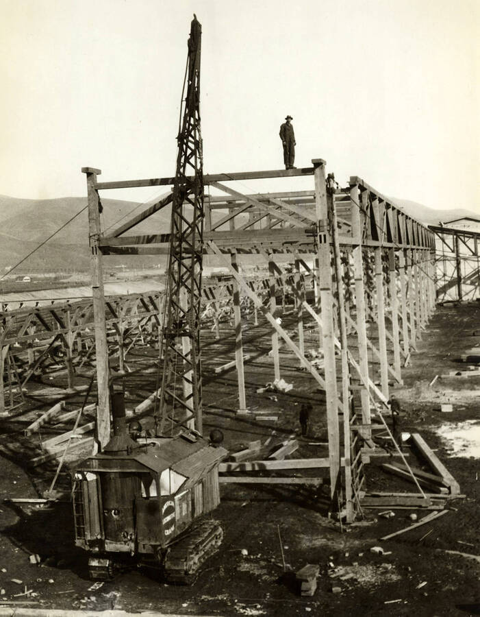 A crane assists with the construction of the buildings at the Lewiston Mill. A Man stands atop the frame.