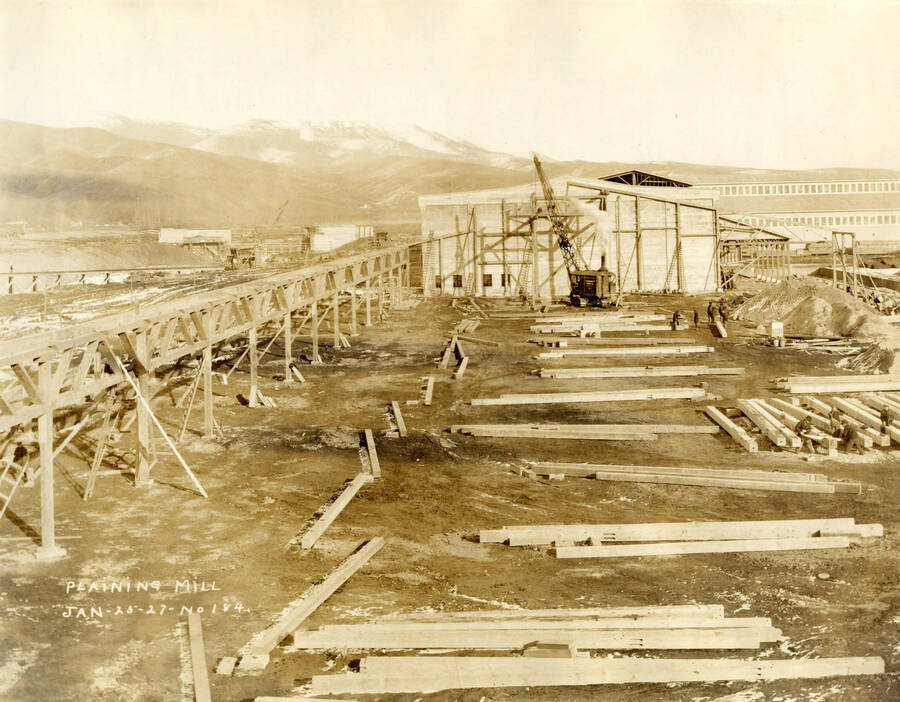A crane assists in the construction of the plaining mill. Piles of lumber lie behind the crane coming towards the camera. Written on the photograph is 'CT CO Planing mill 1/26/1927 No. 184.'