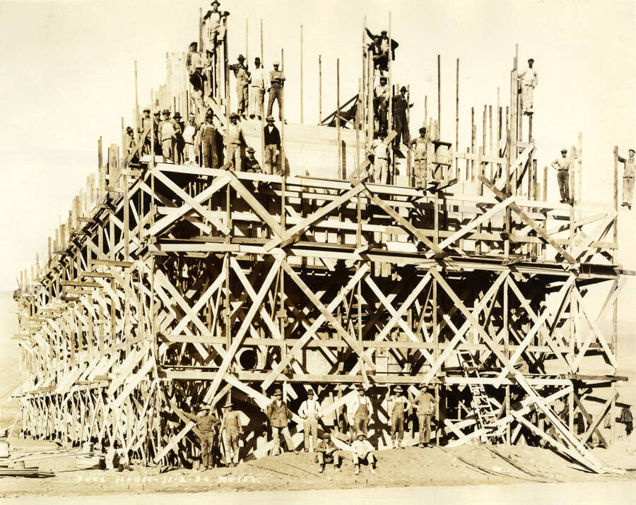 Men stop construction to pose for a picture standing on the framing of the fuel house. Written on the picture is 'Fuel House 11/2/1926 No. 154.'
