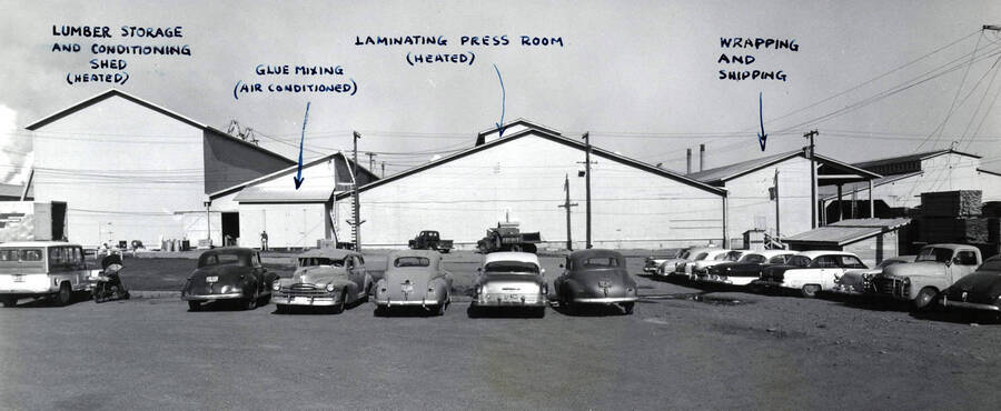 The four buildings of the laminating department at the Clearwater Paper Mill. Cars and a motorcycle sit in the parking lot in front of the buildings. Each building is labeled. From left to right they are:  Lumber storage and Conditioning Shed (Heated), Glue Mixing (air conditioned), Laminating Press Room (heated), and Wrapping and Shipping.