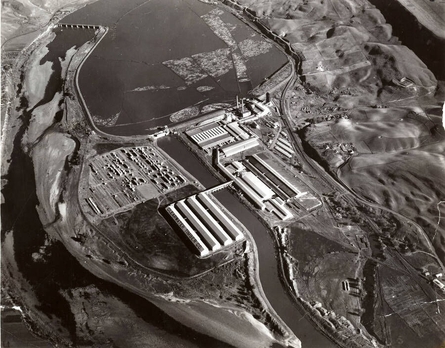 Aerial photograph of the Clearwater Mill. Show in the photographer are the Lewiston Dam towards the top of the photograph, the log pond to the right of the dam, and the mill in front of the pond. Written on one of the buildings is "Clearwater Timber Co."