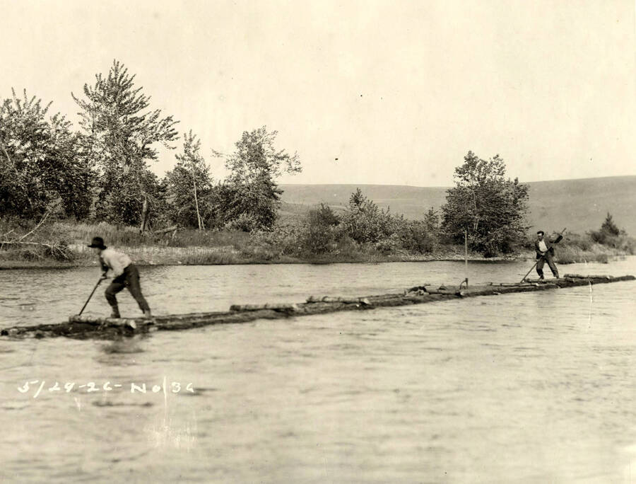 Two men ride a log raft. Written on the photograph is '5/29/1926 No. 36'