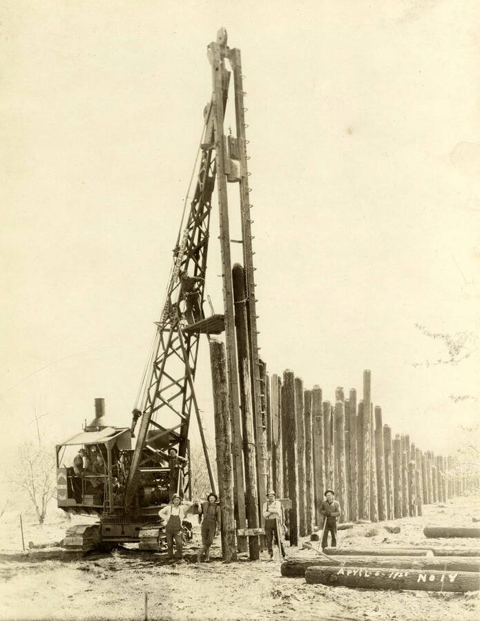 A pile driver attached to a crane is shown while the men using the equipment pose for the picture. Behind them is a row of logs. Written on the photograph is '4/6/1926 No. 14'
