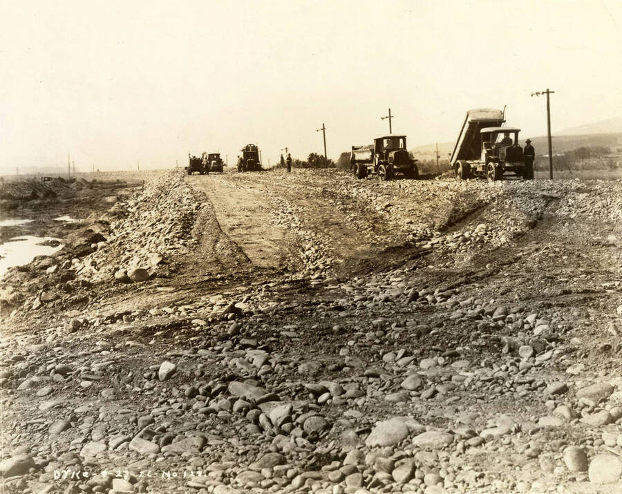Dump trucks dump rock and dirt to build up the dike at the Lewiston Mill. Written on the photograph is 'Dike 9/27/1926 No. 128'