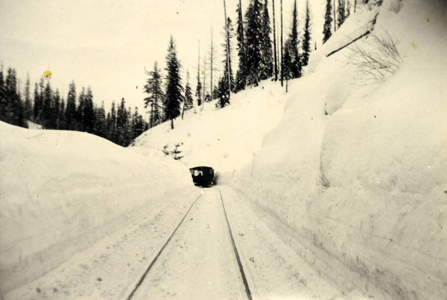 The camp 14 speeder coming up grade from 14 towards Headquarters, Idaho. The snow walls on either side of the track were almost as hard as rock except for a thin outside covering of fresh snow. Width of the plowed trough was only that of a log flat and men walking the track must needs climb the banks in quick fashion when a trainload of logs came past.'