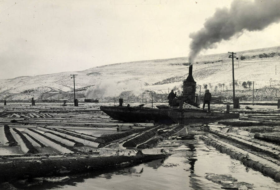 'In the pond proper there were six or seven inches of ice. Log trains were arriving none too promptly from the woods because of deep snow and it was necessary for two shift operation to break loose some of the logs in the large pond. Accordingly an ice breaking barge was rigged up with a steam donkey mounted amidships. Lines were anchored on opposite piers and by means of a winch, driven by the donkey, the barge was pulled back and forth over the logs and ice. the old barge was plenty heavy with its steel plated bottom and upward beveled ends to do the ice breaking job. in fact it kept getting heavier as the water from the pond seeped through cracks in its sides and finally one night disappeared from view under the waters of the pond. Next morning only the smokestack of the donkey engine was visible. However, the ice breaker was speedily salvaged and returned to service.'