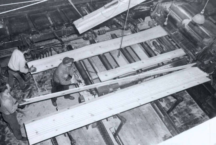 Three men work running straightening out cut planks. Written on the back of the photograph is "Deer Park Pine Industry, Inc. March 8, 1963."