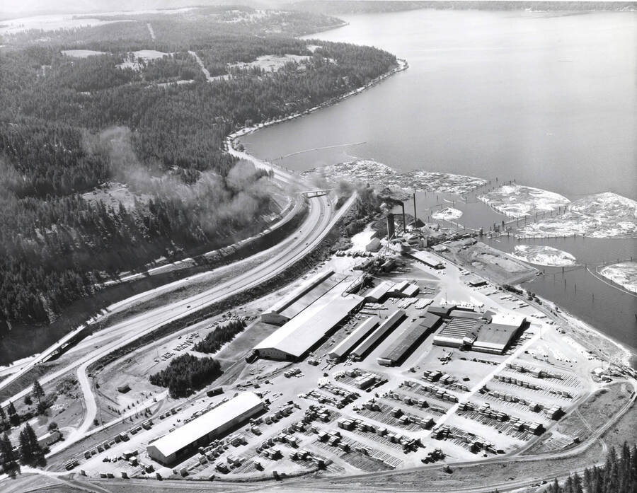 Aerial photograph of the Rutledge Sawmill. In this view, the entire mill can be seen. To the upper right of the mill, are the log ponds and Lake Coeur d'Alene. To the left of the mill is Interstate 90. Stamped on the back of the photograph is: 'Western Ways, Inc. Aerial Photographic Specialists  275 Vera Drive Corvallis Oregon, Phone 35266'