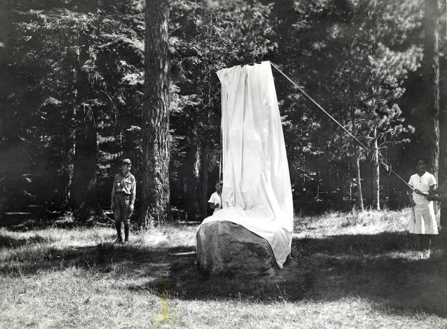 A young boy stands to the right of the monument while two girls stand behind it. Another boy stands to the left read to pull the fabric cover off the monument. The back of the photograph reads 'Dedication of Laird Park August 21, 1937