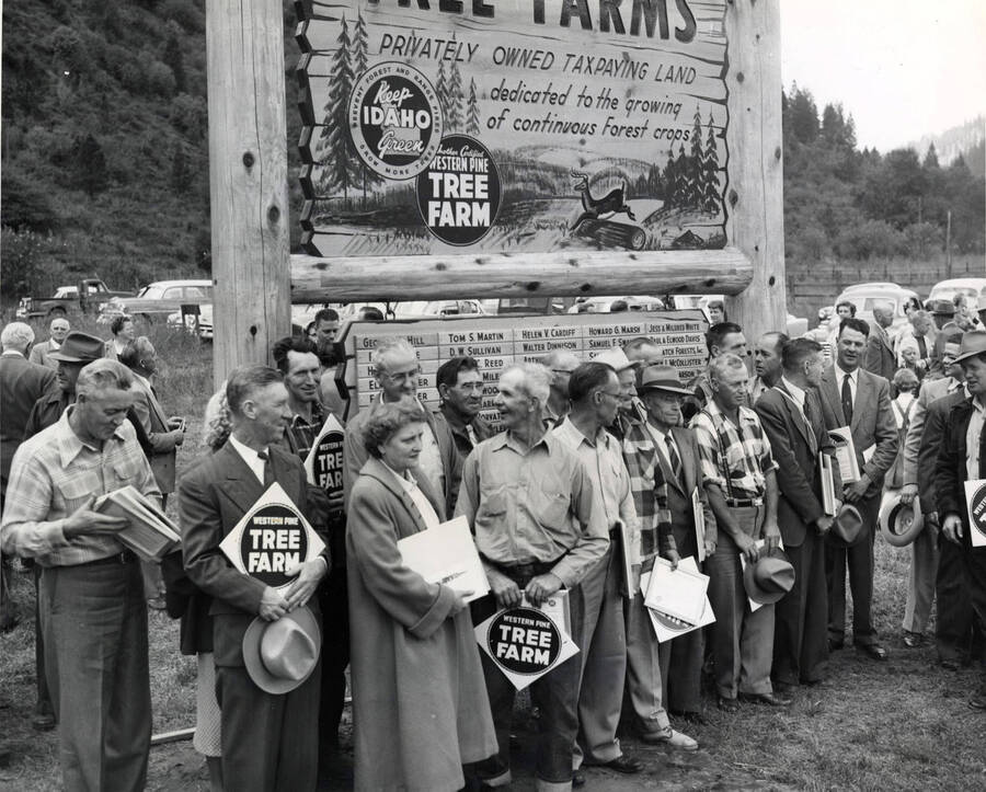 Men and women receive certificates at the Keep Idaho Green meeting. Several men and women are holding a placard that reads 'Western Pine Tree Farm'. Behind the group of people is a sign for Palouse Valley Tree Farm and a list of names.