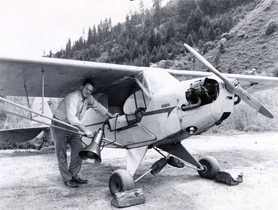 A man stands underneath a Piper plane holding a speaker.