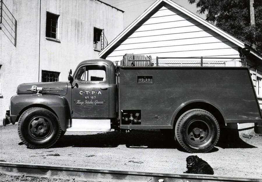 A fire engine truck. On the door to the cab, are the initials "C.T.P.A (Clearwater Timber Protective Association) No. 167 and Keep Idaho Green" On the top of the truck is the hoses. Laying in front of the truck is a dog.
