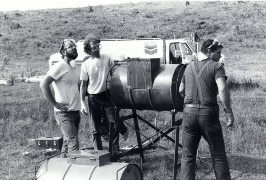 Three men work with a holding tank in preparation for a controlled burn. A Chevron truck can be seen in the background.