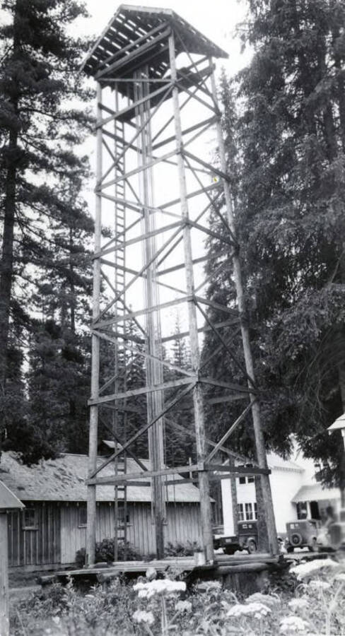 A wooden fire lookout. In the background is a pickup and another automobile.
