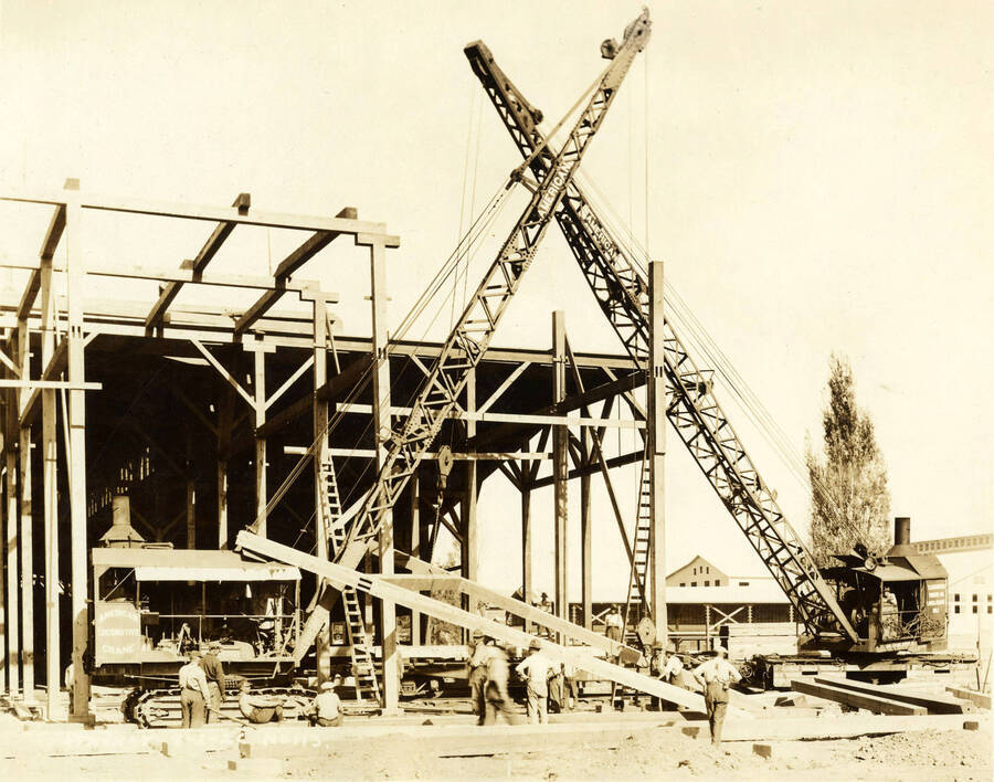 Two cranes work to lift up framing for one of the buildings at the Lewiston Mill. Written on the photograph is 'Stacker 9/2/1926 No. 113'