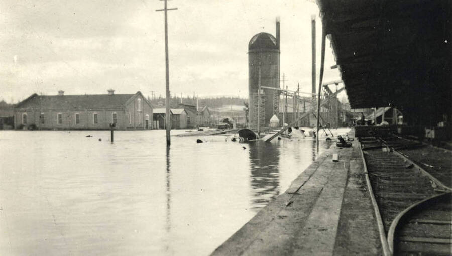 Postcard of Potlatch flooding. On the right side of the picture are railroad tracks, while in the background is a barn and grain silo.
