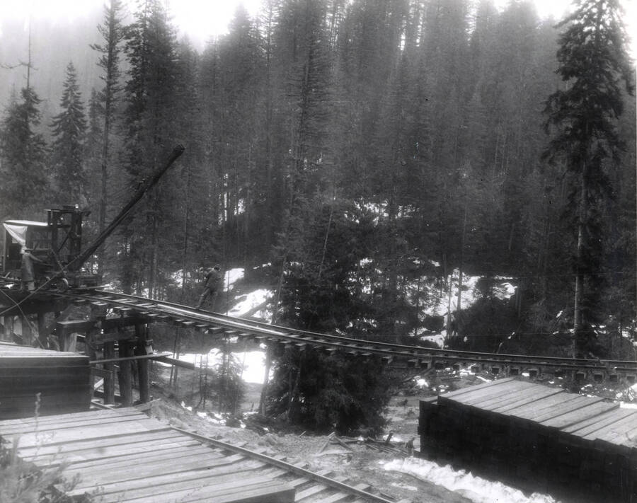A man hangs on to a cable as he looks over the edge of damaged railroad tracks.