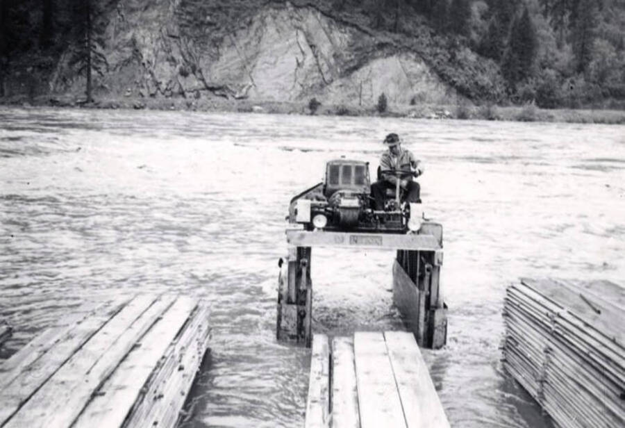 A man sits on top of a piece of mill machinery during the 1948 flood. In front of him are three sets of finished lumber