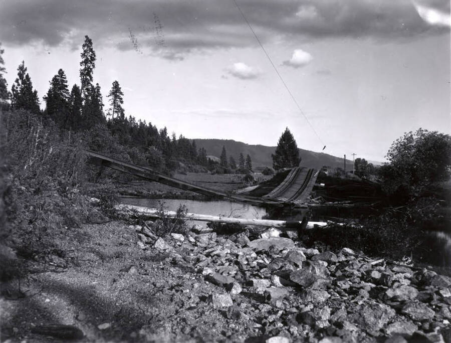 A railroad bridge is damaged and the tracks droop towards the water after the 1948 flood.