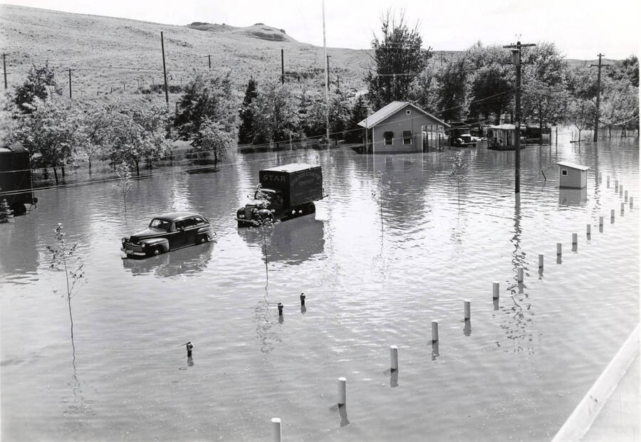 A car and a truck sit the flood waters. A hose with another truck are in the background.