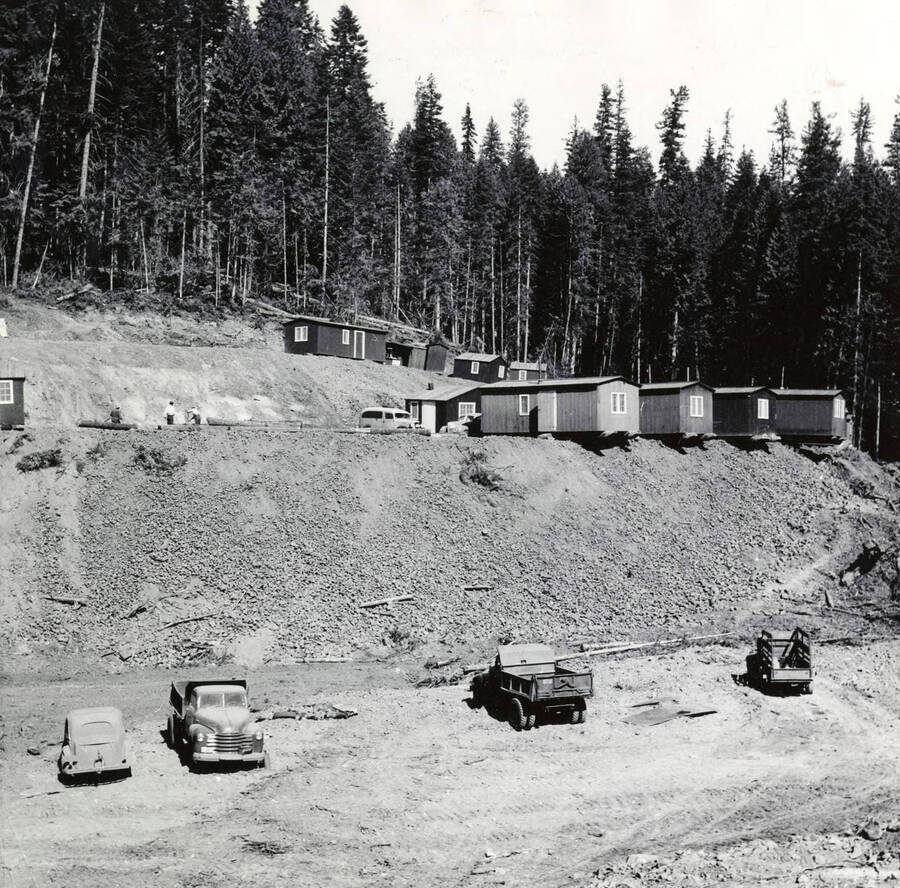 The buildings of Camp Y. On the first two tiers are buildings. Three men work on the second tier. Below the two tiers are several trucks and a car. Written on the back of the photograph is "Camp Y - Sept. 1948 (B.A.)."