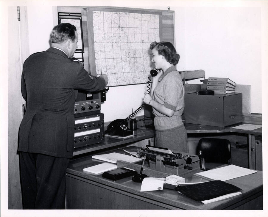 Sgt. George Webster explains use of map while Cerryal Coulter uses telephone at radio communication center in Lewiston administrative offices of PFI. Phone connects with Spokane Filter Center. (Description taking from the back of the photograph)