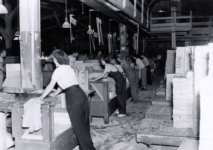 Women work alongside men, sawing planks of wood.