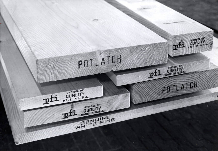 End of planks of wood stamped with the Potlatach name. The stamps read: "Potlatch," "pfi Symbol of Quality made in the USA," "Genuine White Pine." On the back there is a stamp for Photograph's by Richards Studios in Tacoma Washington.