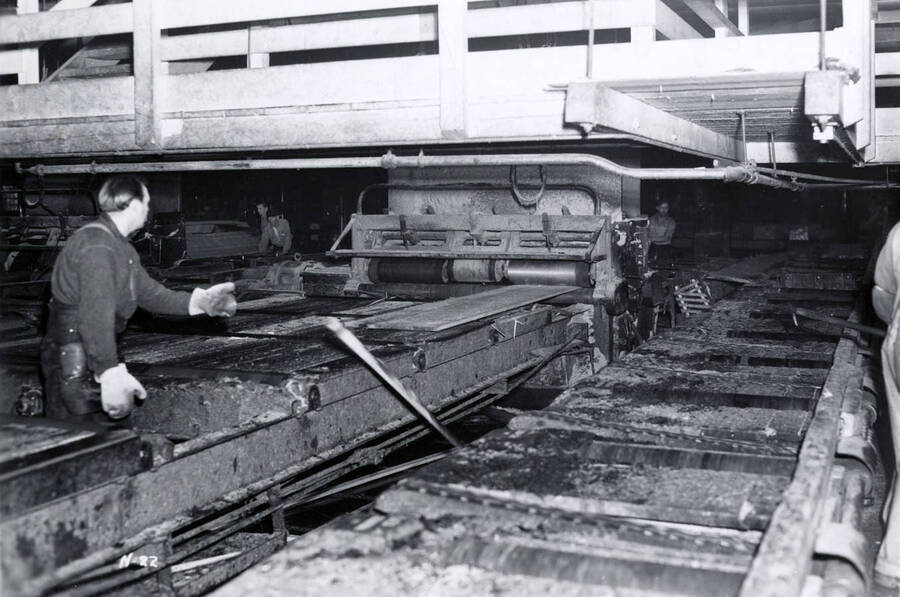 A man works on the edger in the sawmill. Writing on the back says "edging pincher."