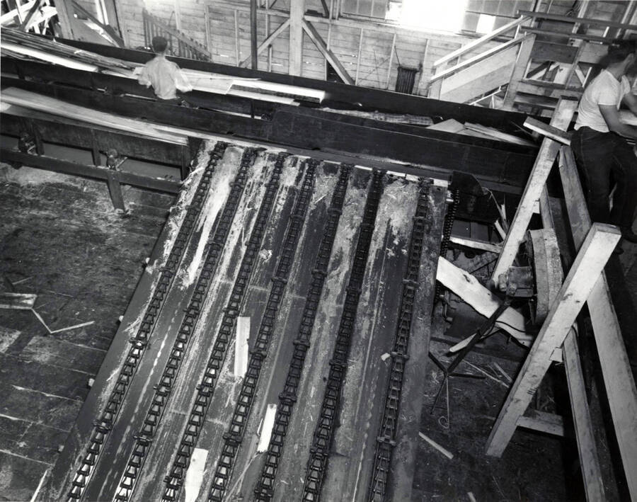 A overhead of the green chain.  At the top of the photo, a worker works with several planks of lumber. On the right hand side towards the top, a worker sits.