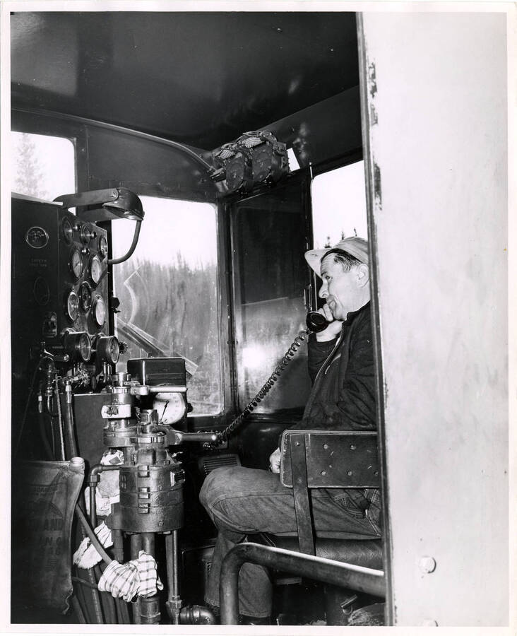 The description on the back of the photograph reads "Engineer George Crystal calls into Headquarters, Idaho from cab of diesel-electric logging locomotive."