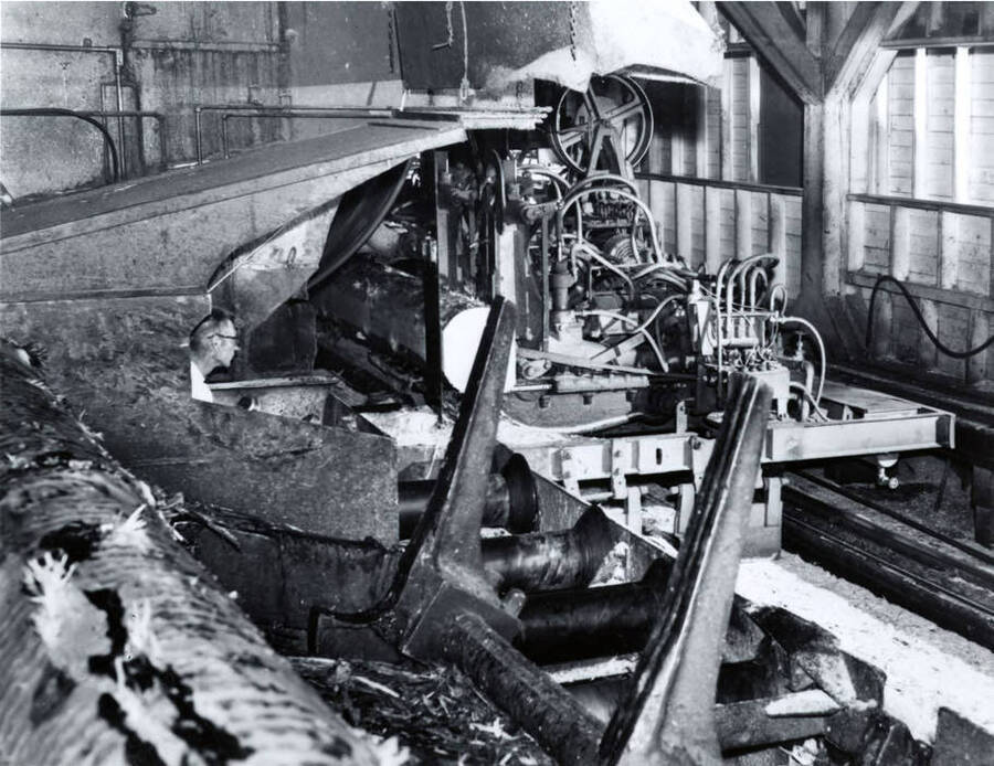 A man operates a piece of machinery at the Clearwater Paper mill. The description on the back of the photograph reads "Head rig operating at the sawmill of the Lewiston, Idaho plant of PFI."