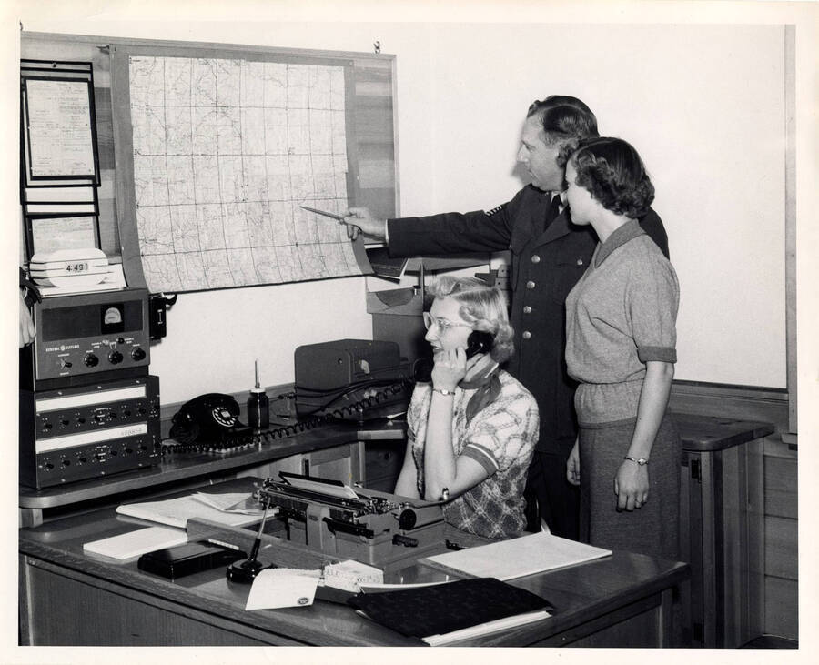 The description on the back of the photograph reads "Operator Bernice Koefelda calls Spokane Filter Center while Sgt. George Webster explains map to Cherryal Coulter."
