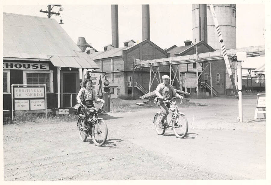 Two employees bicycling away from plant entrance.
