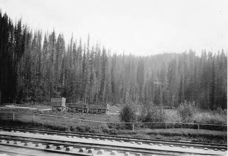 Looking across the railroad tracks towards the site of Headquarters, ID. Three stacks of lumber sit on stilts. Written on the back of the photograph is 'Headquarters 1930s'.