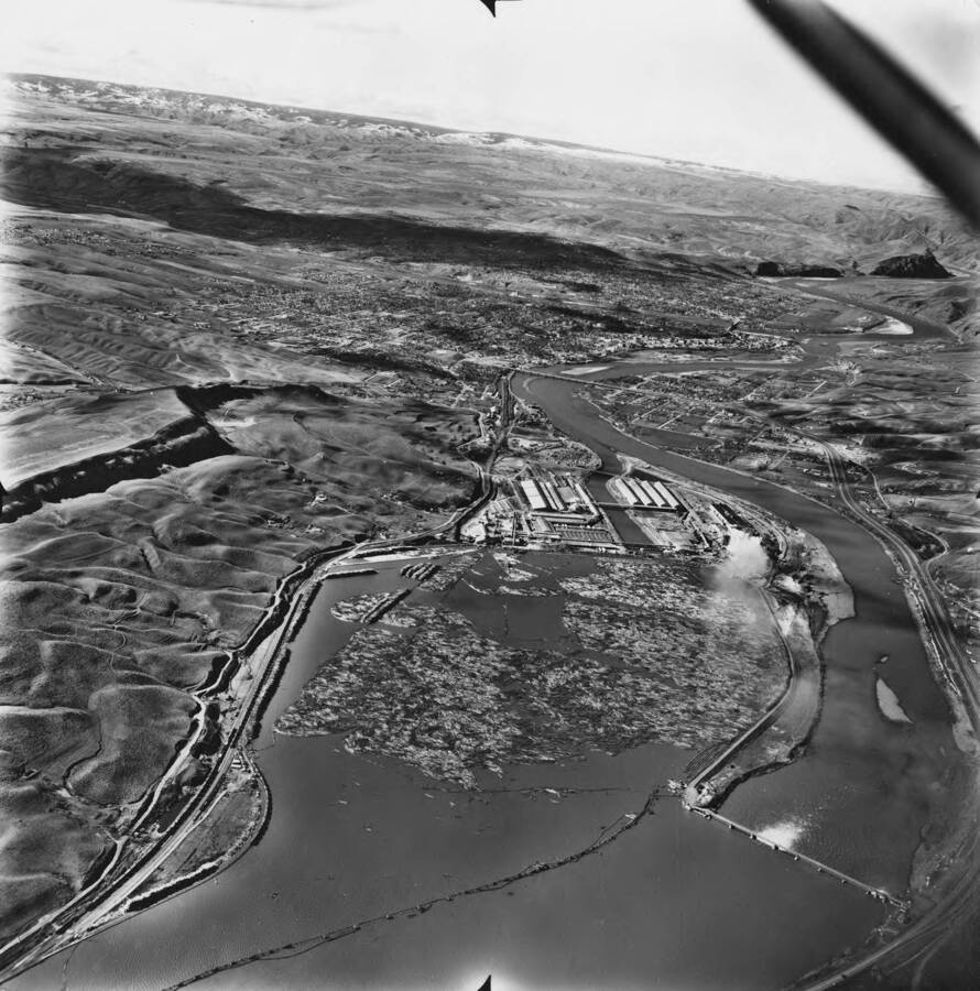 An aerial photograph looking west towards Lewiston, Idaho and Clarkston, Washington and over the Potlatch Mill. In the lower right hand corner is the dam over the Clearwater river.
