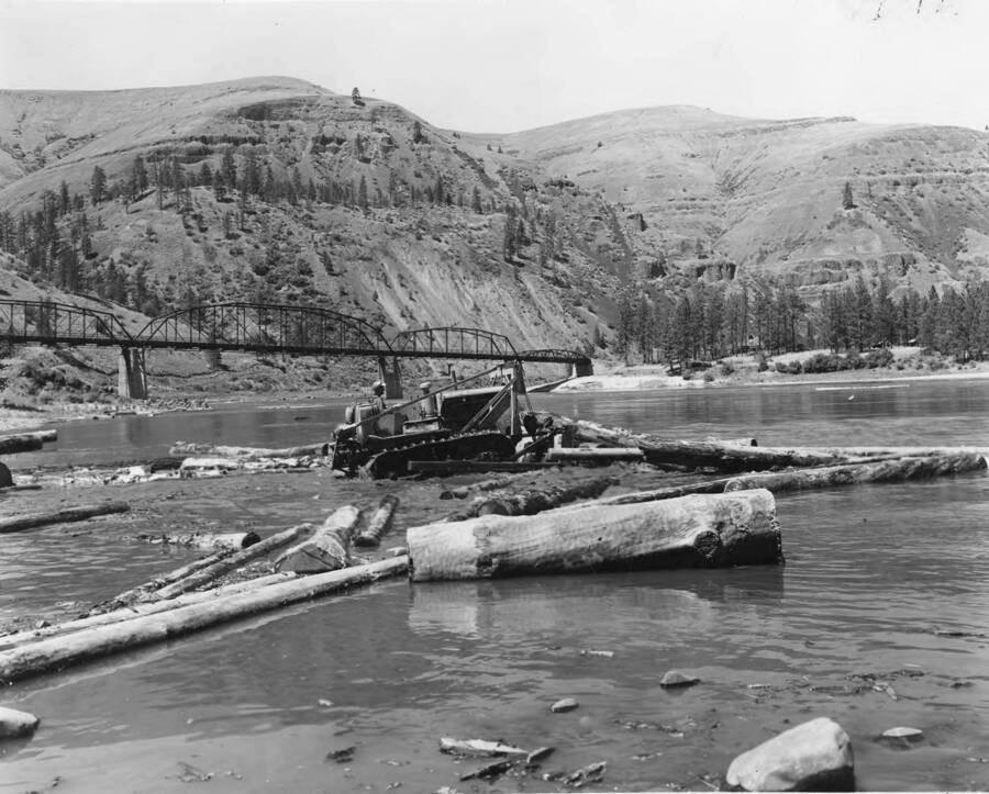 A bulldozer pushes logs into the river to be moved downstream.