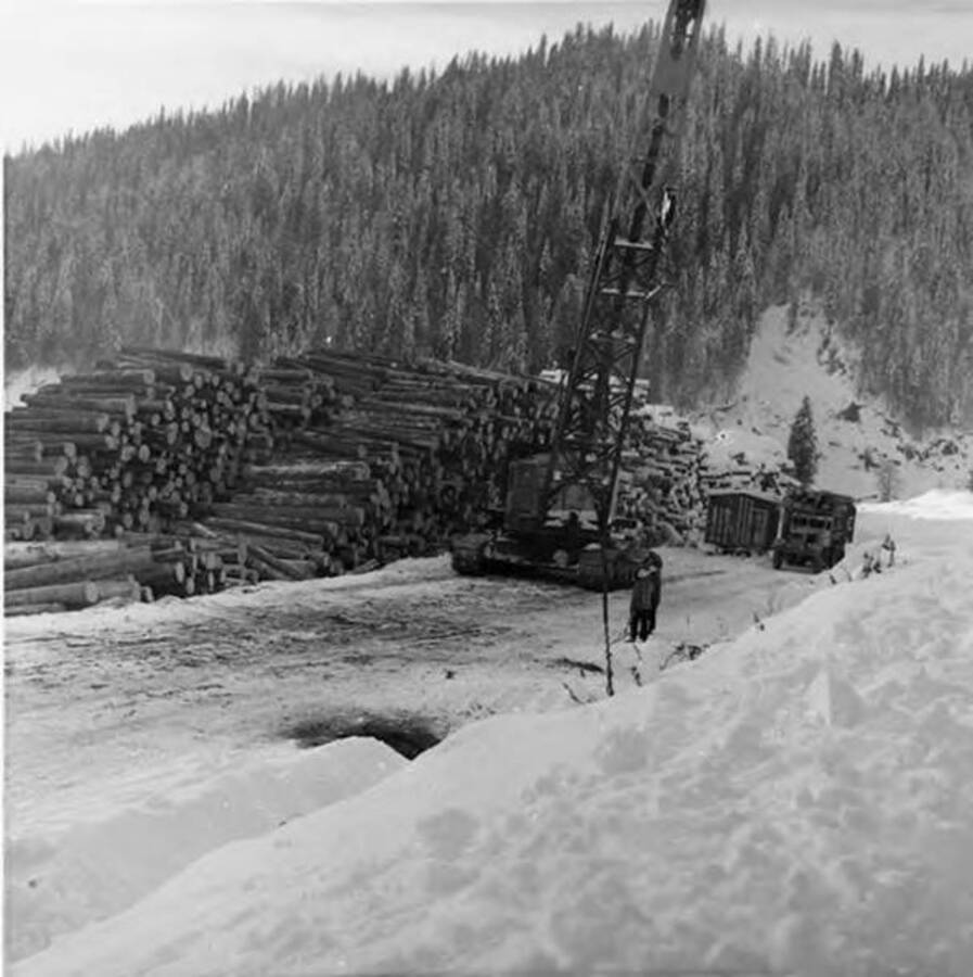 A crane stands waiting for a load of logs to be placed on the deck. Snow can be seen all around the deck and equipment.