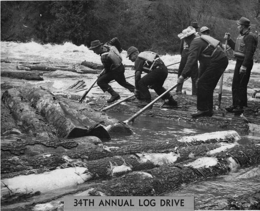 men wearing life vests use peavies to push logs back into the river on the 34th annual log drive.