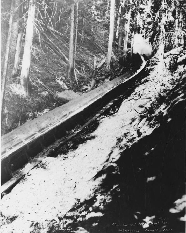 Water creates splash as a log comes down the flume at Camp H. The description on the back of the photograph says '40% grade on Camp H flume Clearwater Timber Co.'