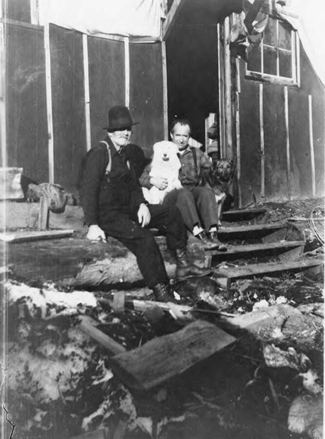 Butch' Nolting and Nick Nollar sit with dogs Snowball and Bob in front of their bunkhouse in Camp 12.
