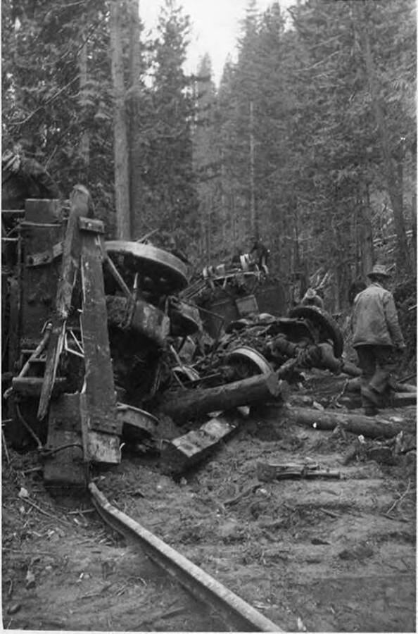 Two men inspect the wreckage of a train tipping off the tracks near camp 14.