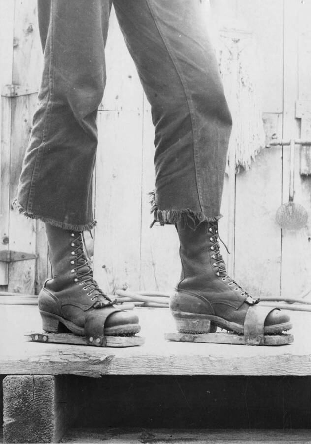 A pair of lumberjack sandals are shown. The description on the back of the photograph reads 'Loggers' sandals worn for noon hour to protect mess hall floors from boot calks.'