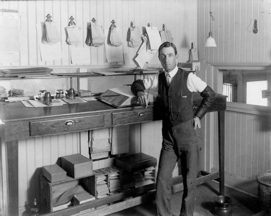 A man stands next to records for the company. The description for the photograph says 'Office of old house (?) - Pat Mere.