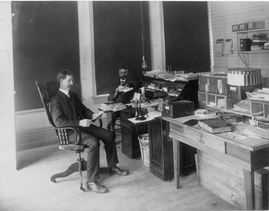 Two men work in the offices of a mill. The description on the back of the photograph says 'left to right A.A. McDonald and Stan Mgn (?).'