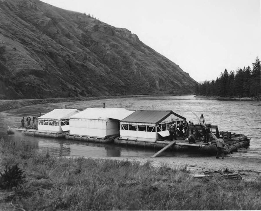 Photograph of the wanigan used for log drives. At the front of the wanigan, a plank of wood goes from the raft to the shore.