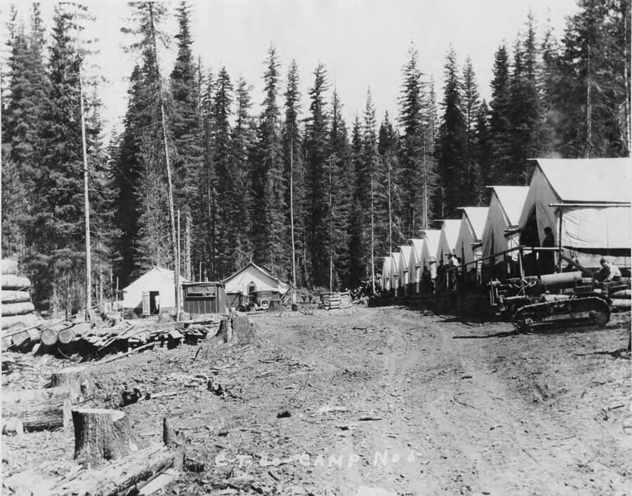 A view of Clearwater Timber Company camp number 6. On the right-hand side of the photograph are the bunk houses. A man sits on an tractor near the last bunkhouse. Other buildings are also visible.