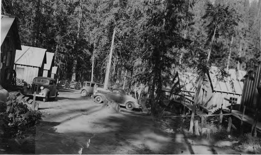 Cars sit in front of bunkhouses. These bunkhouses unlike other camps were made to be more of fixtures rather than the moveable types of bunkhouses in other camps.