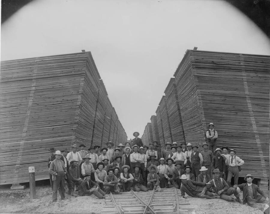 A group of mill workers pose next to stacks of board lumber.